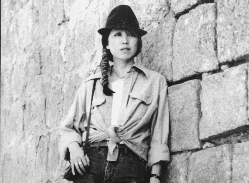 Kirjailija Sanmaon kuva. Kuvassa nuori nainen nojaa kivimuuriin ja katsoo kamerasta ohi.